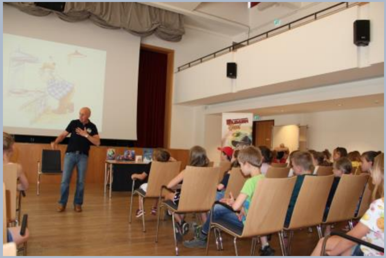 Wolfgang Lambrecht bei seiner Autorenlesung im Bürgersaal mit Kindern auf Stühlen vor ihm.