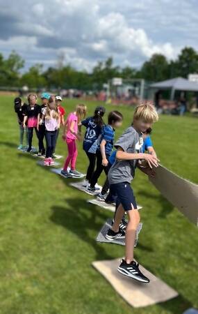 Kinder stehen auf Teppichfließen hintereinander und spielen das Eisschollen-Spiel.